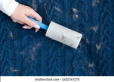 Woman hand using a sticky roller to clean fabrics - woolen knitted sweater from dust, hair, lint and animal fluff, top view, close up.