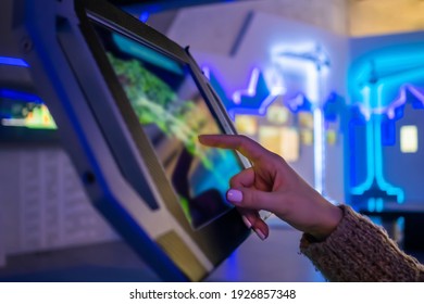 Woman hand using touchscreen display of floor standing tablet kiosk with city map in dark room of museum or exhibition with sci-fi interior: close up side view. Navigation, journey, technology concept