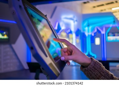 Woman Hand Using Touchscreen Display Of Floor Standing Tablet Kiosk With City Map In Dark Room Of Museum Or Exhibition With Sci-fi Interior: Close Up Side View. Navigation, Journey, Technology Concept