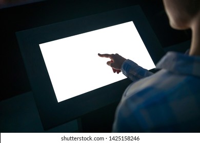 Woman hand using white blank interactive touchscreen display of electronic multimedia kiosk in dark room - scrolling and touching - close up view. Mock up, copyspace, template and technology concept