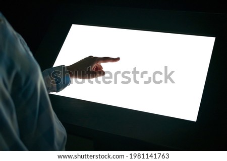 Woman hand using white blank interactive touchscreen display of electronic multimedia kiosk in dark room - scrolling and touching - close up view. Mock up, copyspace, template and technology concept