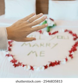 Woman hand wearing a diamond ring after say YES with message WILL YOU MARRY ME made of flower petals with bouquet on bed. Idea for marriage proposal, romantic surprise, wedding and engagement concept - Powered by Shutterstock