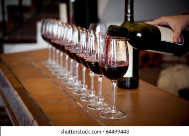 Woman Hand With Wine Bottle Pouring A Row Of Glasses For Tasting