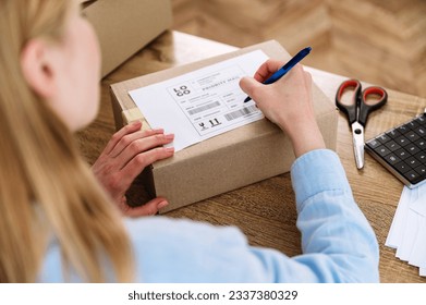Woman hand writing address for delivery, filling information on parcel box. International shipping products to customers. Carton package with label. Fast logistic service.