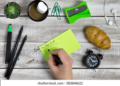 Woman Hand Writing To Do List, Aerial View. Green, Black And White Themed Wooden Desk.