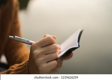 Woman Hand Writing Down In Small White Memo Notebook For Take A Note Not To Forget Or To Do List Plan For Future. 