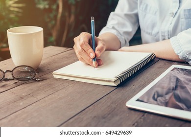 Woman Hand Writing Note Pad On Wood Table In Coffee Shop