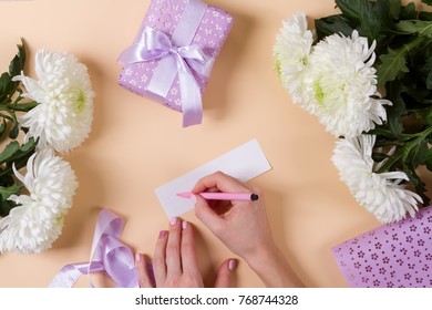 Woman Hand Writing A Note With The Text Thank You On A Paper, Over Beige Table And Flowers