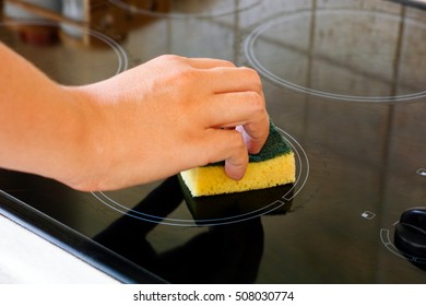 Woman hand with yellow sponge cleaning ceramic hob.