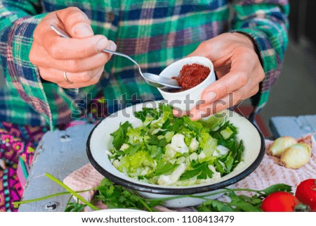 Woman hands adds ajika paste to vegetables green salad. Adzhika - traditional Georgian caucasus hot spicy sauce made with tomatoes, chilly pepper and coriander. Raw vegan vegetarian food