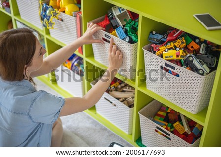 Woman hands applying printing sticker with name title of children toys for comfortable sorting and storage at home. Caring mother organizing domestic space for kids. Housekeeping and household