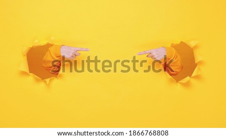 Woman hands arm pointing on copyspace isolated through torn yellow wall orange background studio. Copy space advertisement place for text image promotional content Advertising area workspace mock up