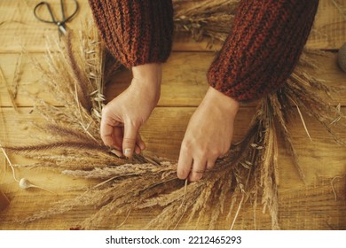 Woman Hands Arranging Dried Grass In Wreath On Wooden Table, Top View. Making Stylish Autumn Wreath On Rustic Table. Fall Decor And Arrangement In Farmhouse