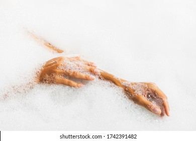 Woman hands in bath full of foam bubbles close-up. Spa beauty treatment.