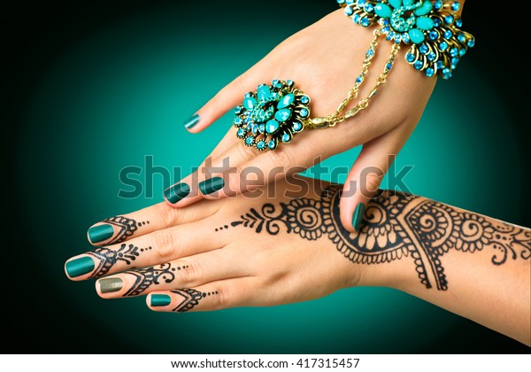 Woman Hands with\
black mehndi tattoo. Hands of Indian bride girl with black henna\
tattoos. Hand with perfect turquoise manicure and national Indian\
jewels. Fashion. India