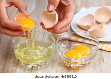 Woman hands breaking an egg to separate  egg white and  yolks and egg shells at the background  