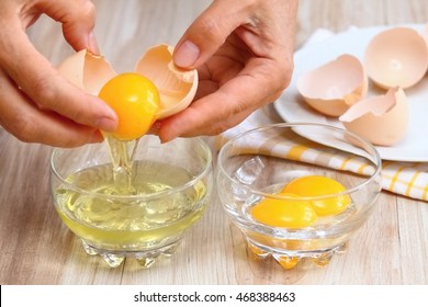 Woman hands breaking an egg to separate  egg  white and  yolks and egg shells at the background  