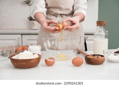 Woman hands are breaking eggs for baking on the table with ingredients: flour, cottage, milk, nuts in light kitchen. - Powered by Shutterstock