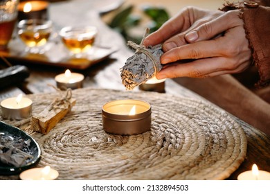 Woman Hands Burning White Sage, Before Ritual On The Table With Candles And Green Plants. Smoke Of Smudging Treats Pain And Stress, Clear Negative Energy And Meditation