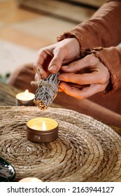 Woman Hands Burning White Sage, Before Ritual On The Table With Candles And Green Plants. Smoke Of Smudging Treats Pain And Stress, Clear Negative Energy And Meditation