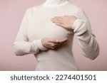 Woman hands checking lumps on her breast for signs of breast cancer on pink background. Healthcare concept.