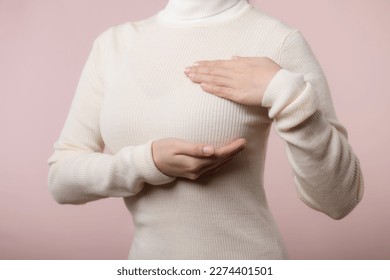 Woman hands checking lumps on her breast for signs of breast cancer on pink background. Healthcare concept.