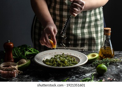 Woman Hands Cooking Penne Pasta And Adding Cheese Parmesan In Dish. Sprinkling With Cheese On Green Pasta With Spinach And Green Pesto.