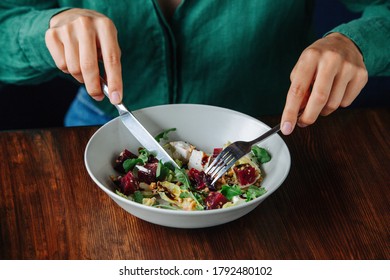 Woman Hands Cutting Exquisite Salad Dish In A Bowl With Fork And Knife. Eating On A Wooden Table. No Head.