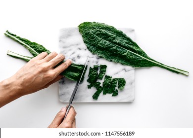 Woman hands cutting organic green kale leaves on a marble board over a white table background, healthy cooking nutrition concept, top view - Powered by Shutterstock