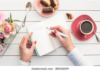 Woman hands drawing or writing with ink pen in open notebook on white wooden table. Bird eye view.