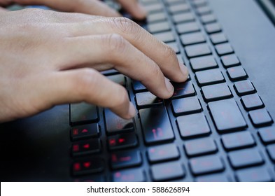 Woman hands and fingers typing on black laptop computer's keyboard with red alphabet on buttons