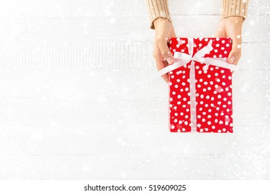 Woman Hands Giving Red Gift Box On White Wood Background With Snowfall