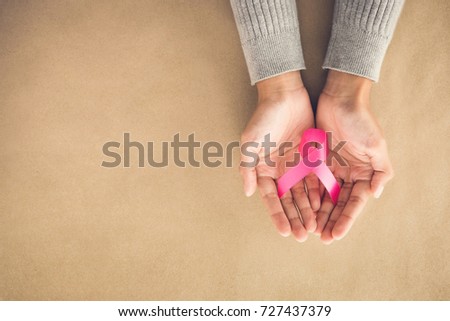 Woman hands giving satin pink ribbon, supporting symbol of breast cancer awareness campaign in October, on light brown paper background with copy space