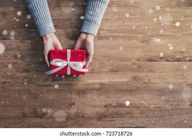 Woman Hands In Gray Sweater, On Wood Table Background,giving Red Christmas Holiday Gift Boxes Top View With Copy Space And Falling Snow Effect