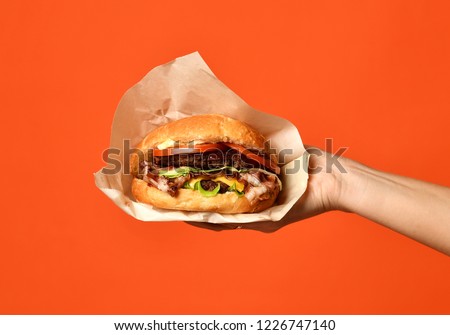 Woman hands hold big cheeseburger barbeque sandwich with marble beef on orange background
