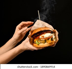 Woman hands hold big craft cheeseburger sandwich with marble beef cheese bacon with steam smoke on black background