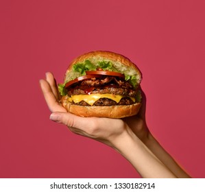Woman hands hold big double cheeseburger burger sandwich with beef tomatoes and cheese on pink  background