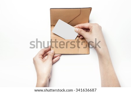 A woman hands hold a brown leather wallet(case, pocket) for passport with a white credit card on the white desk(table) top view isolated white at the studio.