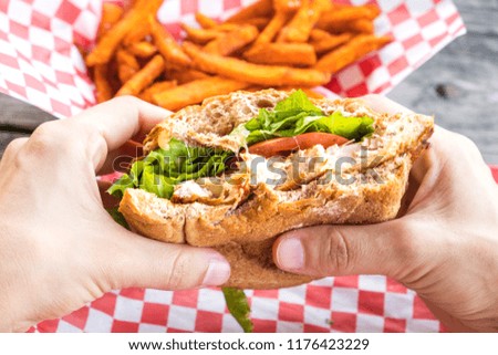 Woman hands hold burger style grilled chicken breast sandwich with lettuce and tomatoes and a side of sweet potato fries