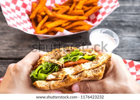Woman hands hold burger style grilled chicken breast sandwich with lettuce and tomatoes and a side of sweet potato fries