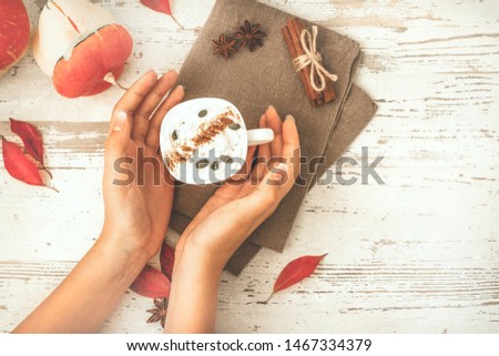 Woman hands hold a cup of spicy pumpkin latte, autumn hot drink white cup, with pumpkins, cinnamon and spices on old rustic wooden background copy space