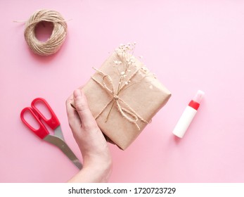 Woman Hands Hold Decoratinng Present. DIY Tutorial Gift Wrapping In Eco Rustic Style On Pink Background. . Сoncept Decorating Gift With Nature Materials, Do It Yourself. Top View