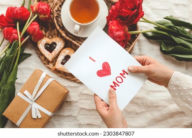 Woman hands holding a beautiful hand drawn Mother's Day greeting card with red envelope, I Love You Mom message on the card. - Powered by Shutterstock