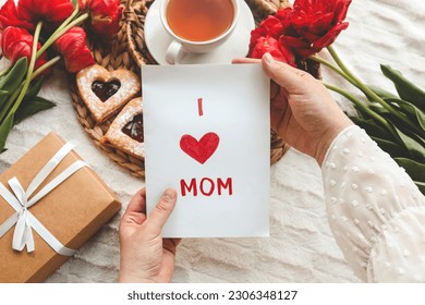 Woman hands holding a beautiful hand drawn Mother's Day greeting card with red envelope, I Love You Mom message on the card. - Powered by Shutterstock