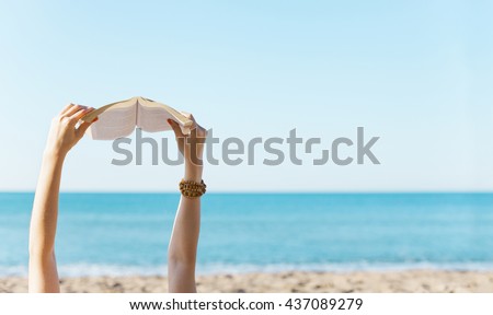 Woman hands holding book with the sea side in background.