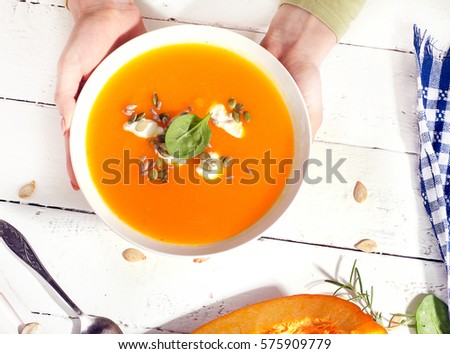 Woman hands holding bowl of healthy pumpkin soup. Top view