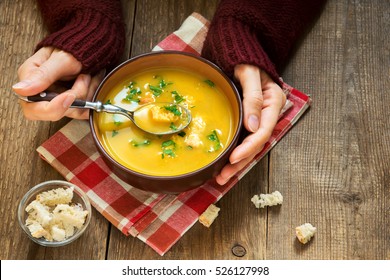 Woman hands holding bowl of vegetable soup with parsley and croutons over wooden background - healthy winter vegetarian food