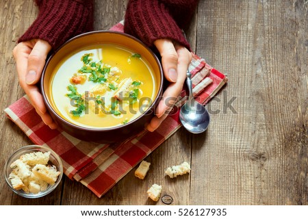Woman hands holding bowl of vegetable soup with parsley and croutons over wooden background - healthy winter vegetarian food