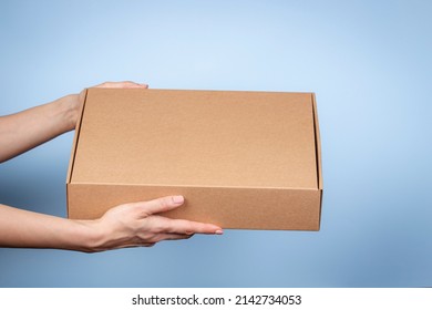 Woman hands holding brown ecological package box made of natural corrugated cardboard. Mockup mailing parcel box on blue background. Packaging, shopping, delivery concept