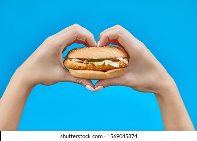 Woman Hands Holding A Burger On A Blue Background.  Two Hands Making Heart Sign With Hamburger 